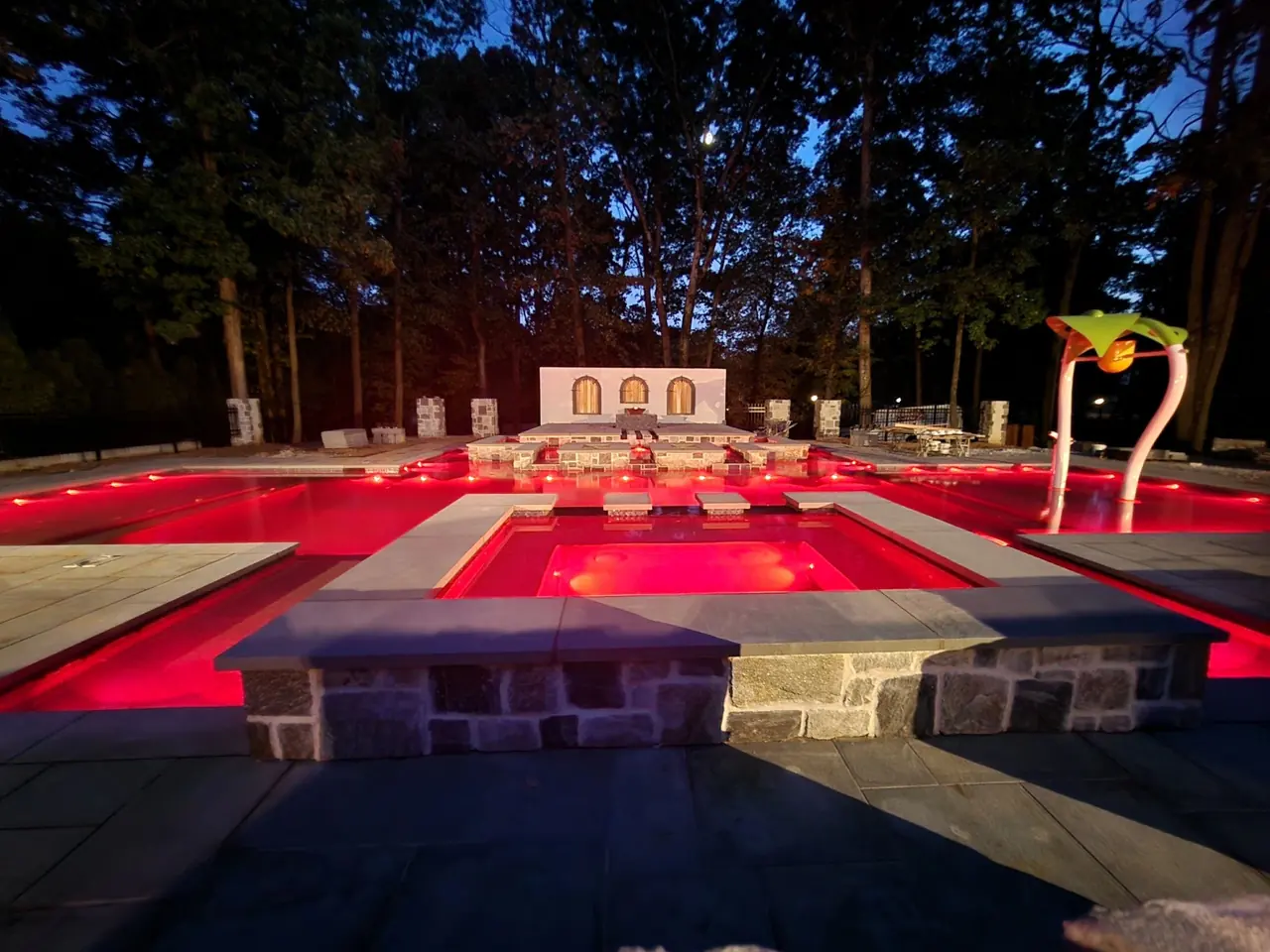 A backyard pool and spa lit in red at night
