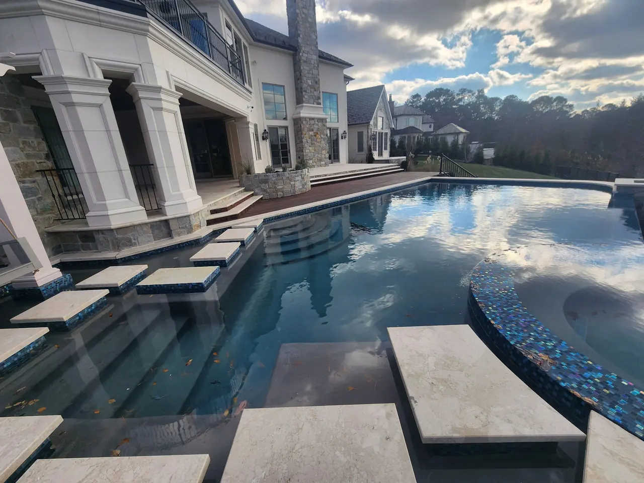 An infinity-edge pool and spa overlooking a lake behind a large home